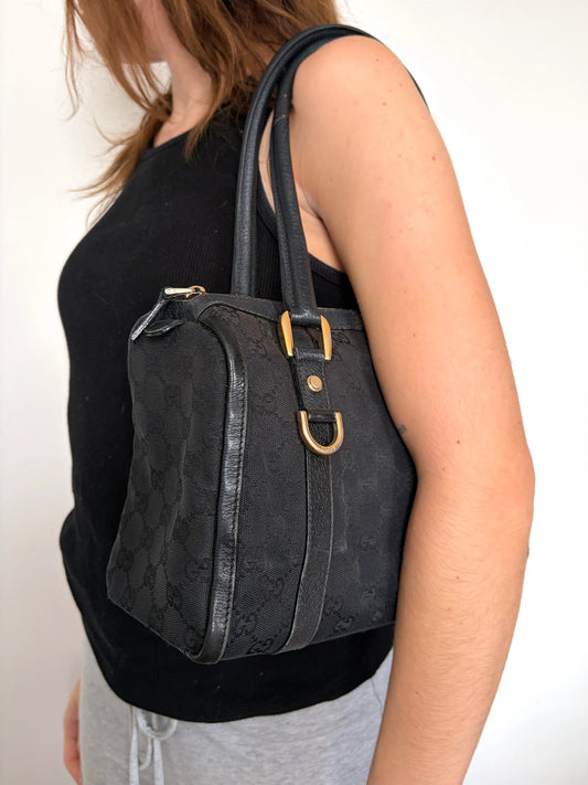 Gucci black GG canvas shoulder bag with gold script logo and engraved D-ring.