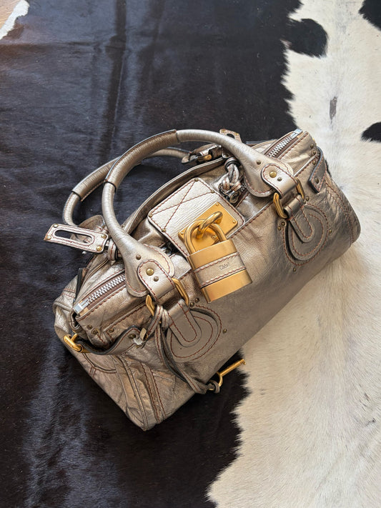 Chloé beige metallic handbag with oversized brass padlock and dual rolled handles.