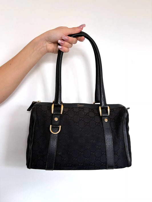 Gucci black GG canvas shoulder bag with gold script logo and engraved D-ring.