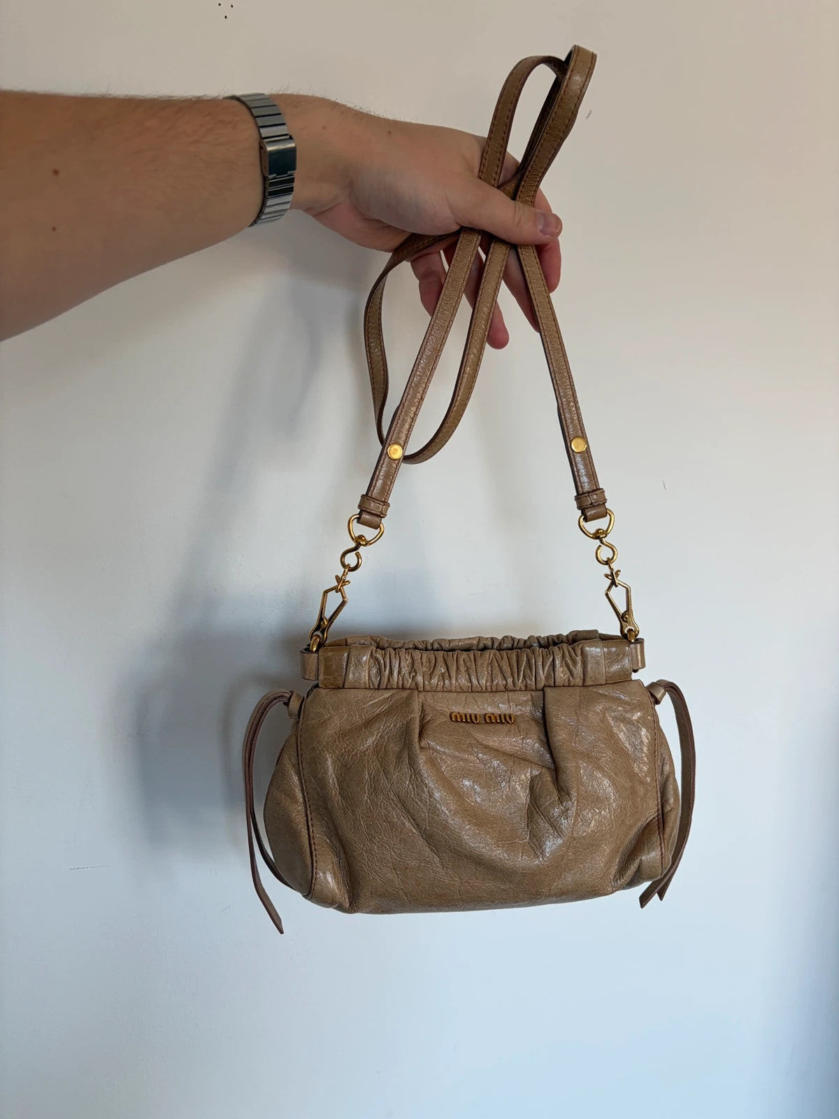 Miu Miu taupe mini crossbody bag with ruched collar, gold lettering, and leather strap.
