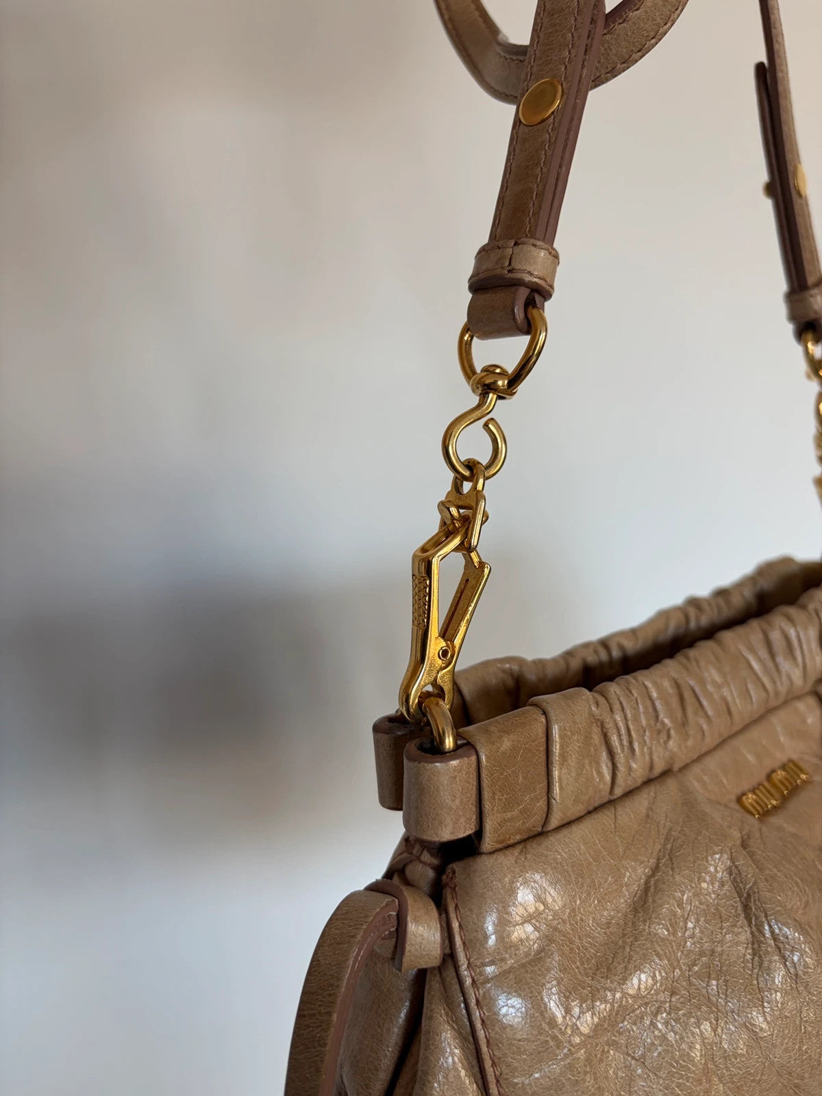 Miu Miu taupe mini crossbody bag with ruched collar, gold lettering, and leather strap.