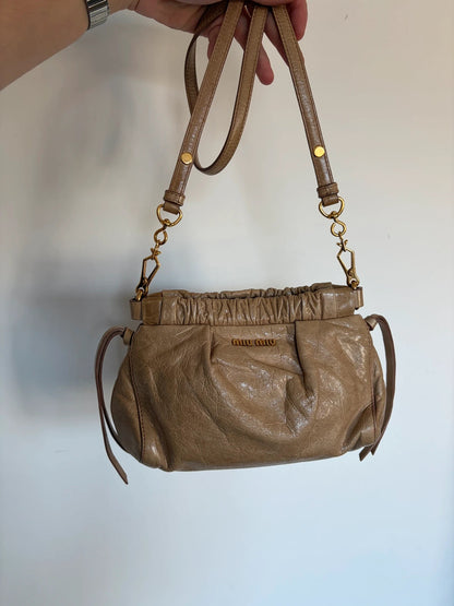 Miu Miu taupe mini crossbody bag with ruched collar, gold lettering, and leather strap.