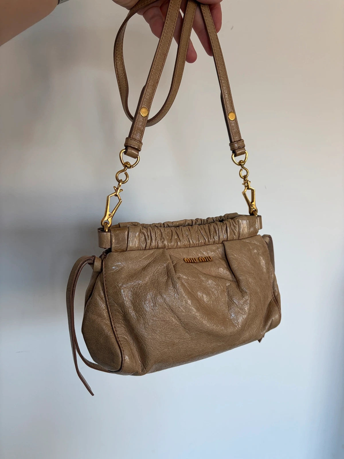 Miu Miu taupe mini crossbody bag with ruched collar, gold lettering, and leather strap.