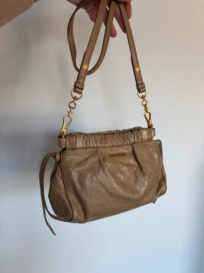Miu Miu taupe mini crossbody bag with ruched collar, gold lettering, and leather strap.
