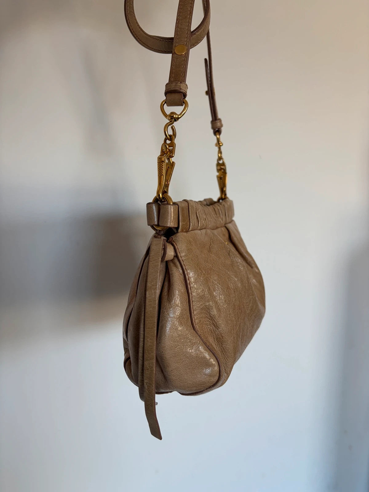 Miu Miu taupe mini crossbody bag with ruched collar, gold lettering, and leather strap.