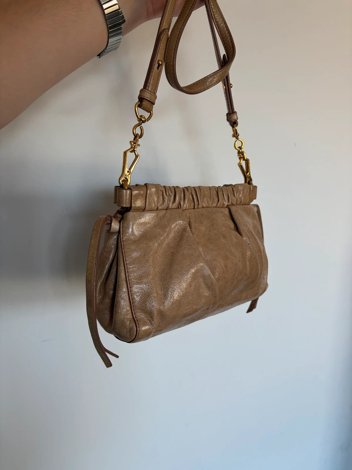 Miu Miu taupe mini crossbody bag with ruched collar, gold lettering, and leather strap.