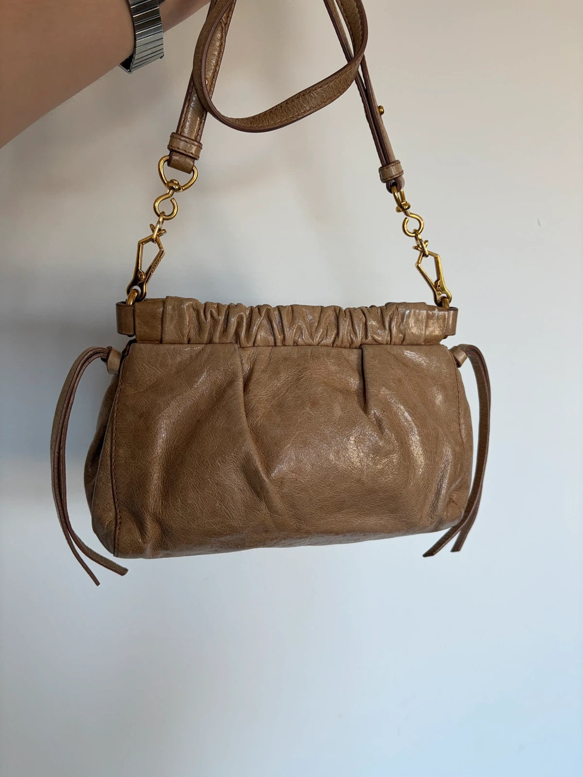 Miu Miu taupe mini crossbody bag with ruched collar, gold lettering, and leather strap.