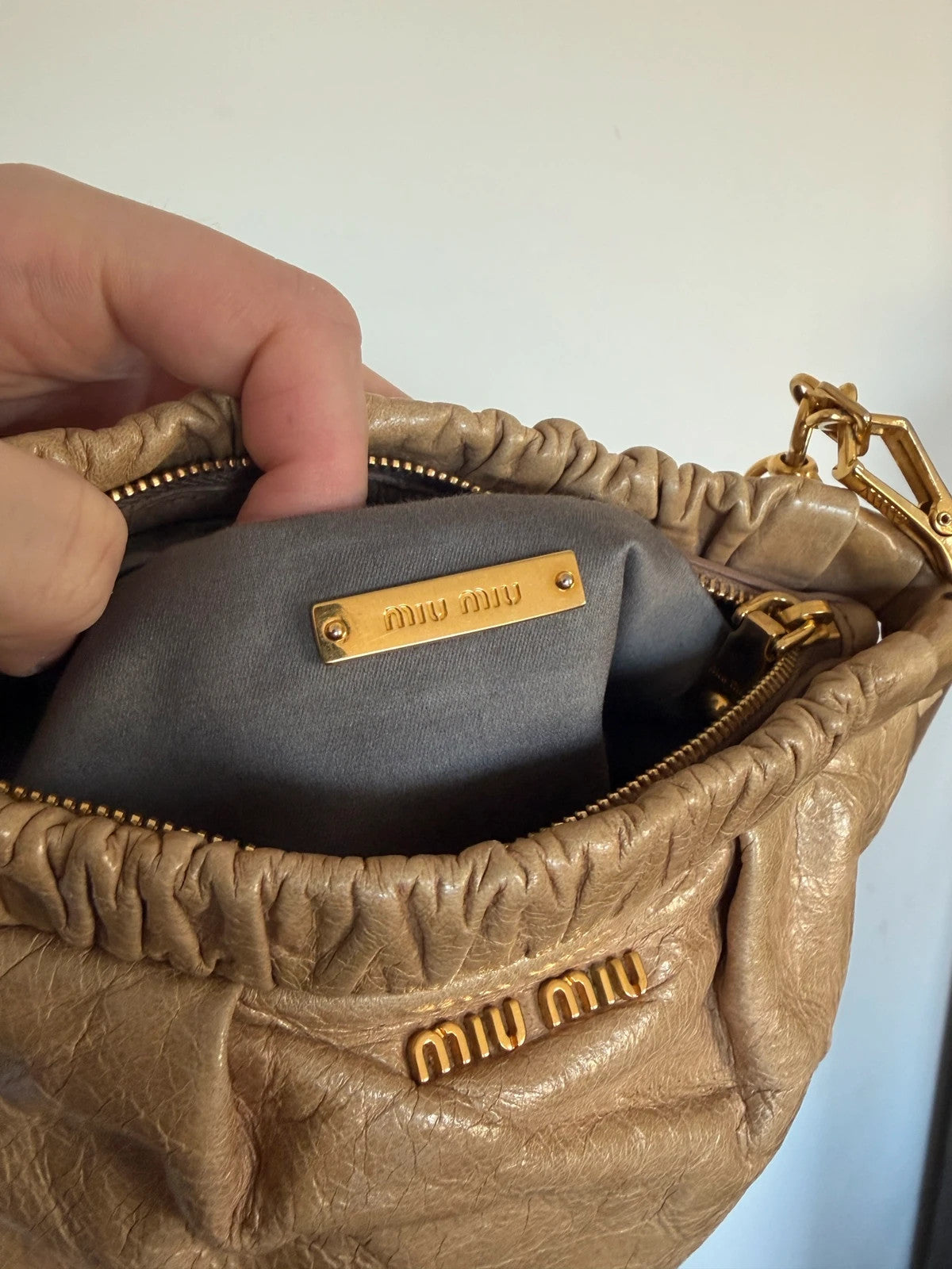 Miu Miu taupe mini crossbody bag with ruched collar, gold lettering, and leather strap.
