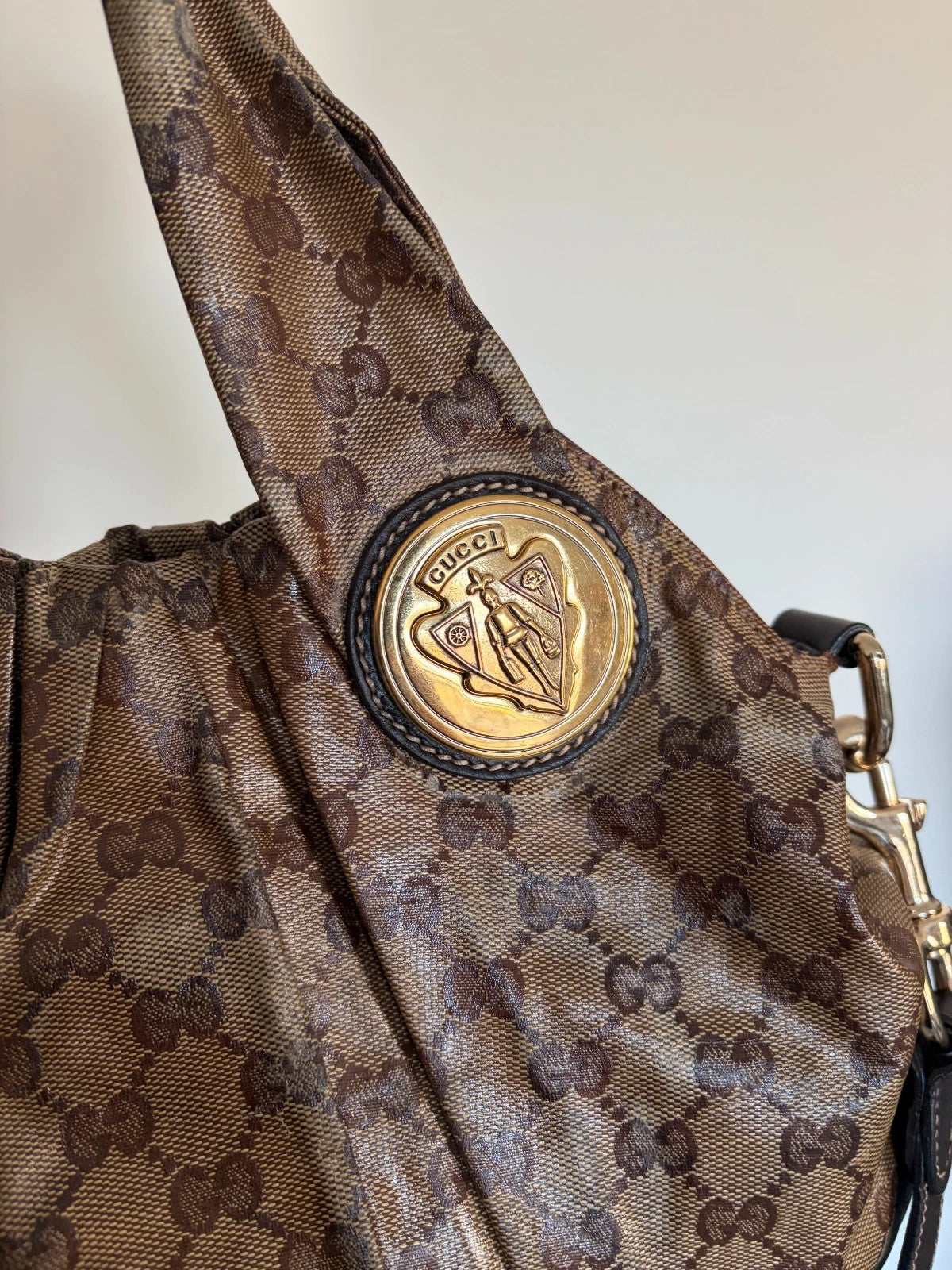 Gucci brown hobo bag with GG monogram, gold-tone knight crest medallions, and leather straps.