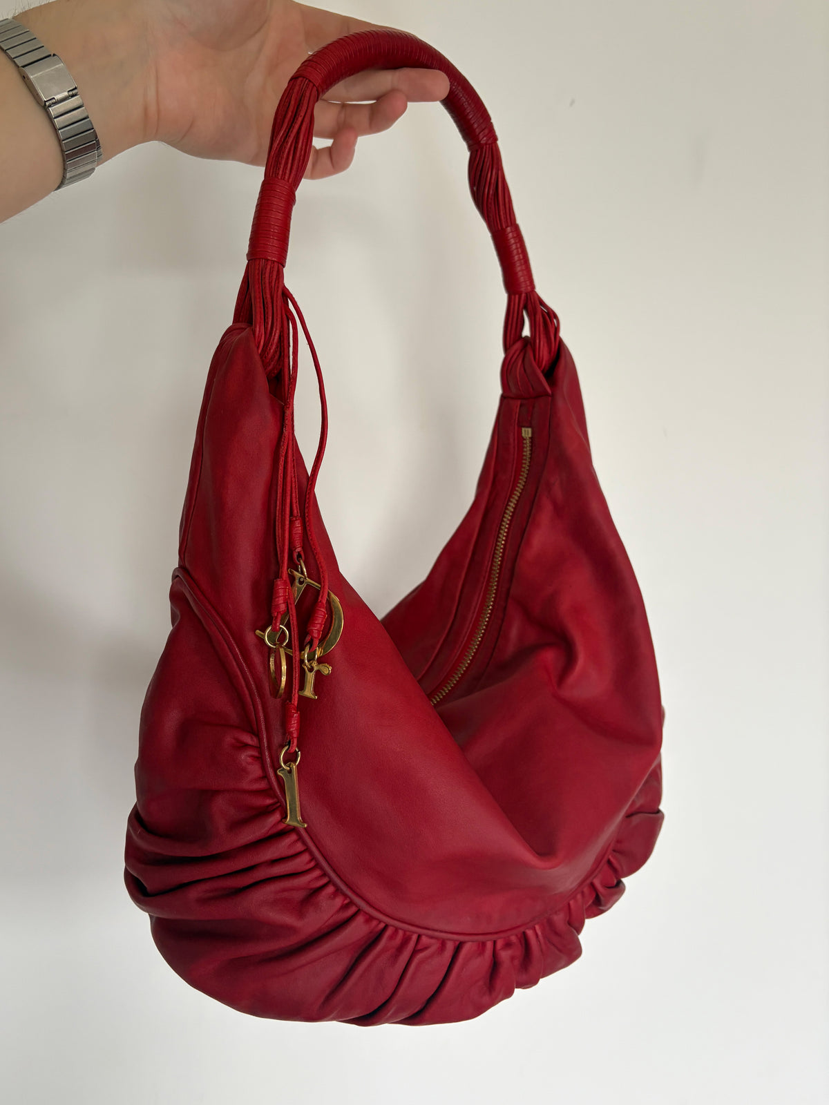 A red leather shoulder bag with gold-tone hardware, held by a hand against a plain white background.