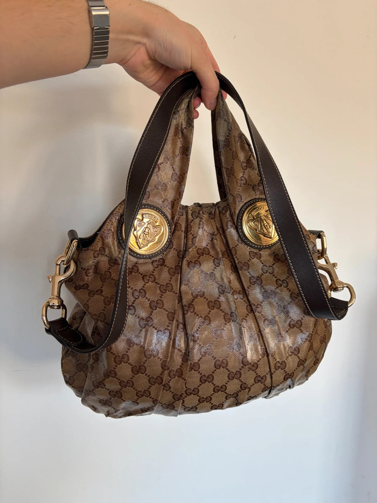 Gucci brown hobo bag with GG monogram, gold-tone knight crest medallions, and leather straps.