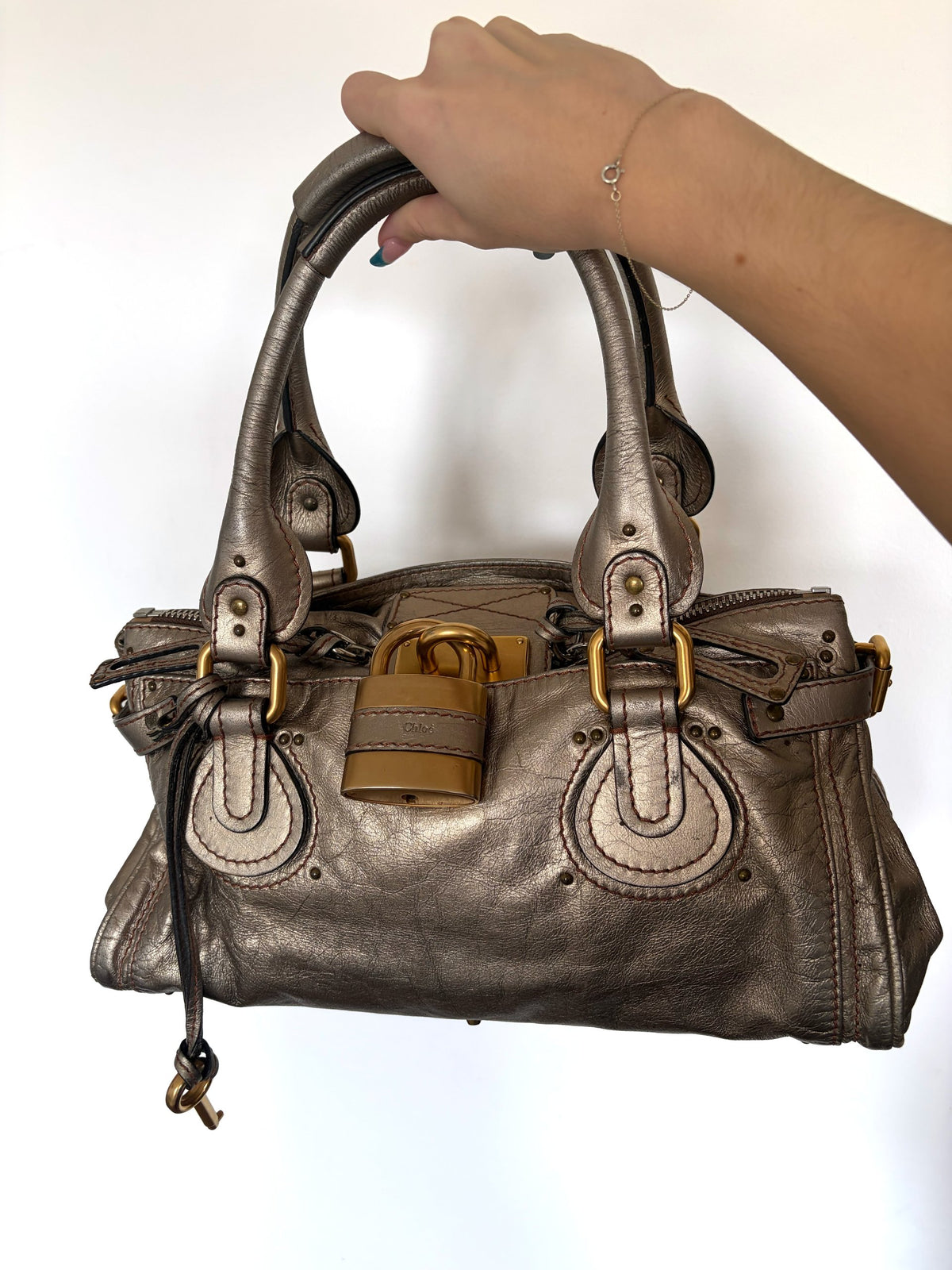 Chloé beige metallic handbag with oversized brass padlock and dual rolled handles.
