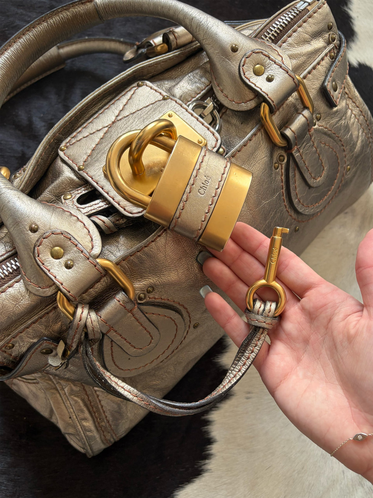 Chloé beige metallic handbag with oversized brass padlock and dual rolled handles.