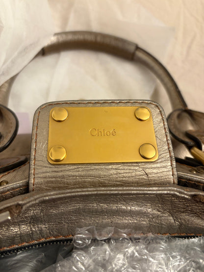 Chloé beige metallic handbag with oversized brass padlock and dual rolled handles.
