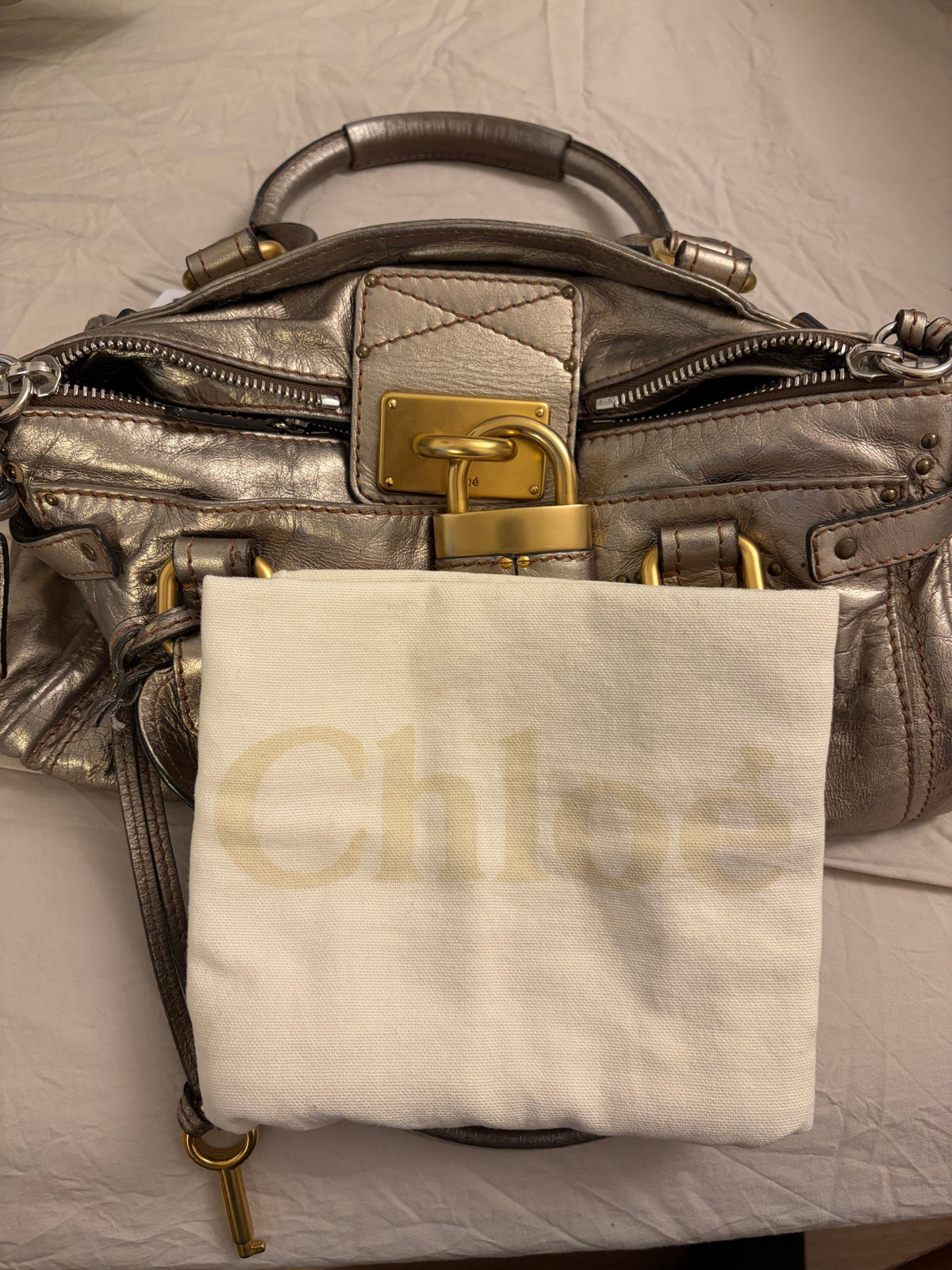 Chloé beige metallic handbag with oversized brass padlock and dual rolled handles.