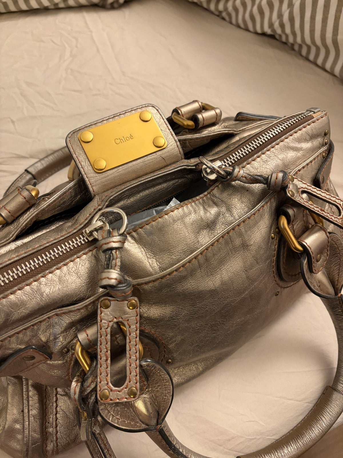 Chloé beige metallic handbag with oversized brass padlock and dual rolled handles.